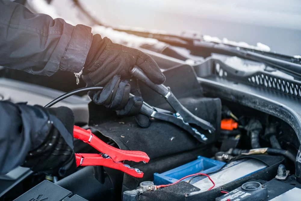 Person in gloves attaching jumper cables to a battery